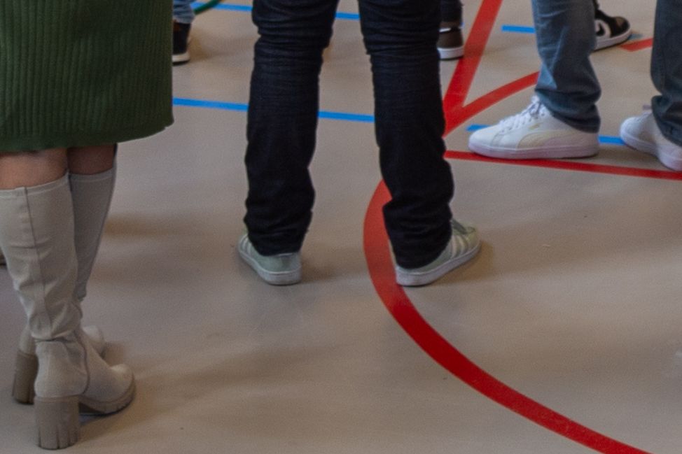 mensen staan opgesteld langs strepen op de grond van een gymzaal.